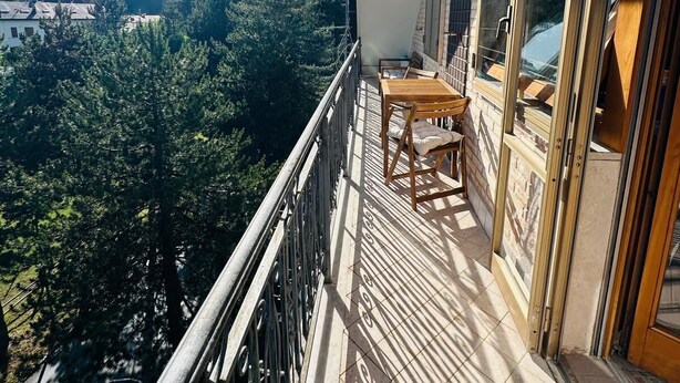 Un balcone con tavolo e sedie, affaccia su un paesaggio montuoso.