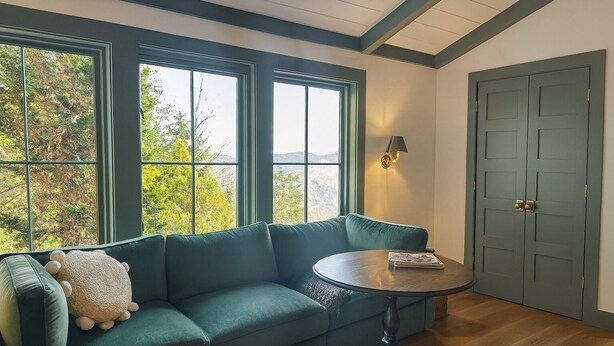 A room with a green sofa, a round wooden table, and a door. - Sapphire Retreat   • Stylish 1BR Suite + Hot Tub, Views, Ski Hill & Outdoor Living (Sapphire)