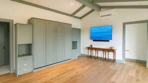 A spacious room with a large wardrobe, a wooden console table, and a mounted TV. - Sapphire Retreat • Stylish 1BR Suite + Hot Tub, Views, Ski Hill & Outdoor Living (Sapphire)