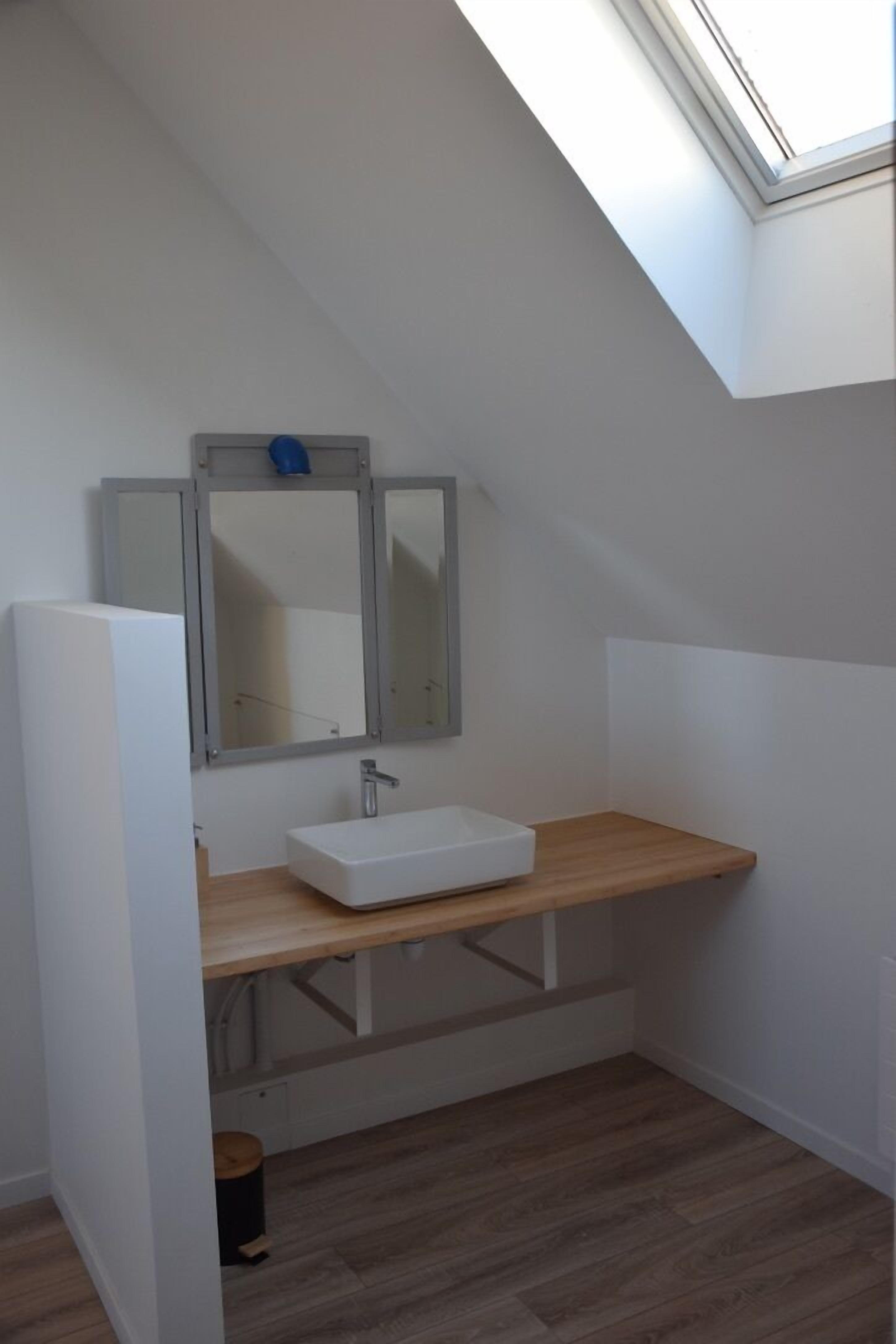 Un bagno piccolo con un lucernario, un lavandino bianco e un mobile vanitario in legno.