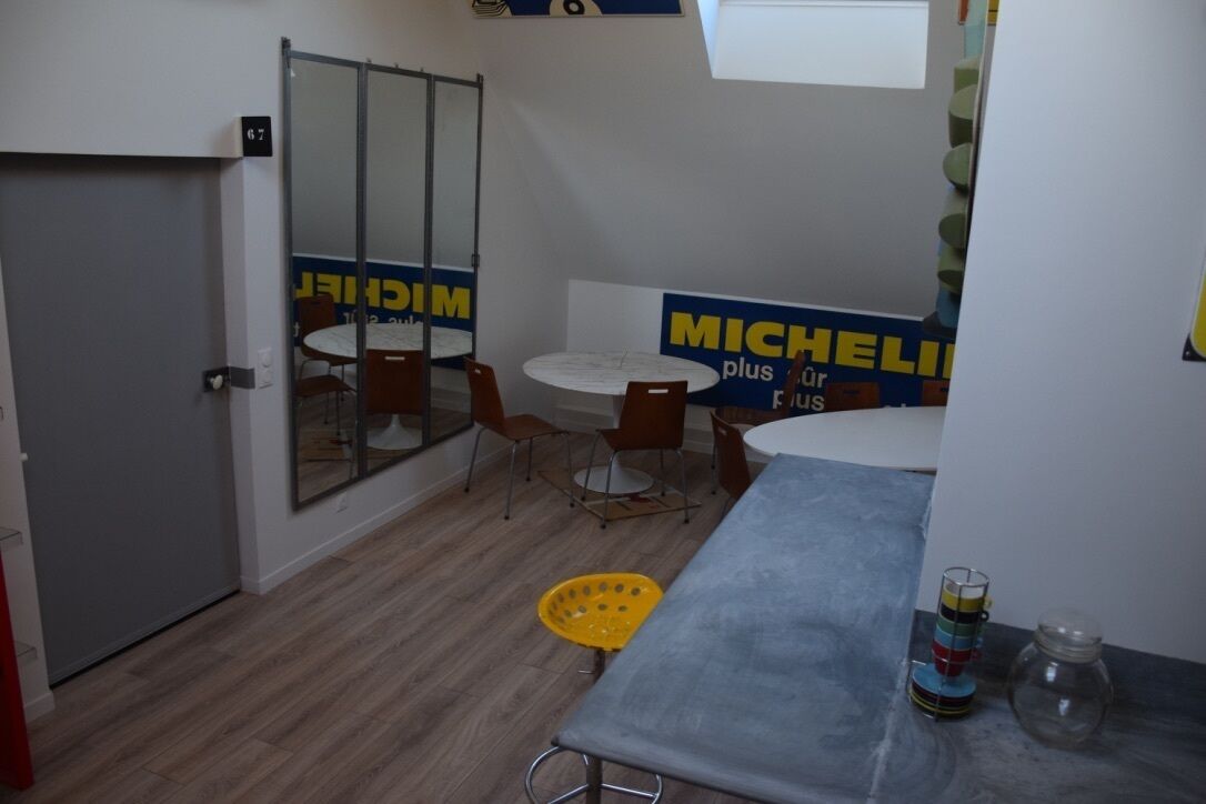 A small room with a door, a round table with chairs, a yellow basket, and a Michelin Plus sign on the wall.