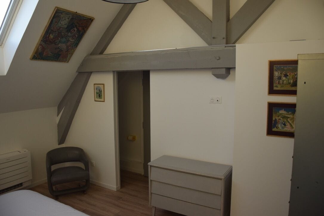 Ett sovrum med ett sluttande tak, en säng, ett skrivbord och en stol. Det finns två tavlor på väggarna och ett element på vänster sida.