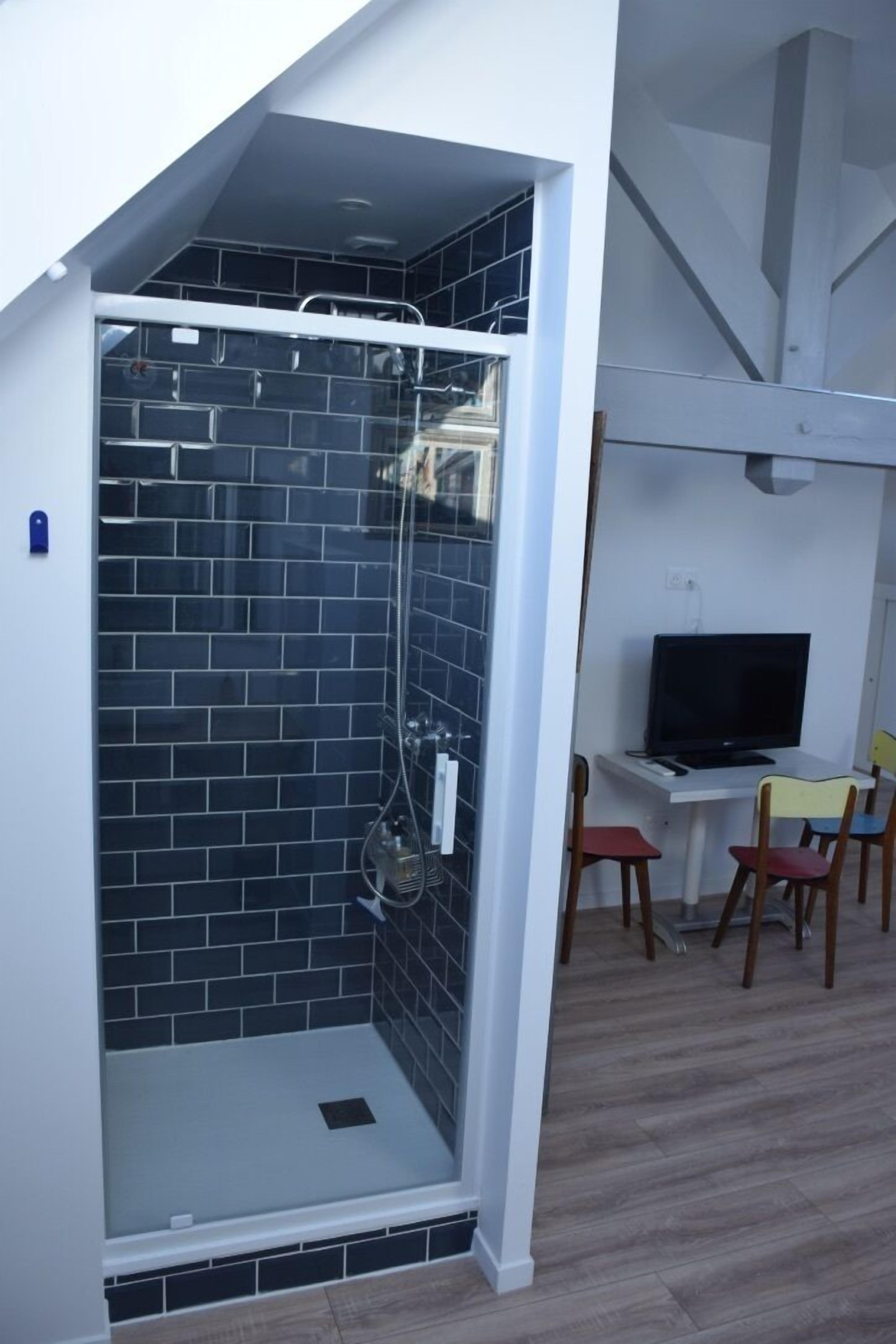 Ein modernes Badezimmer mit einer Duschkabine aus Glas, einem weißen Waschbecken und einem Fernseher auf einem kleinen Tisch.