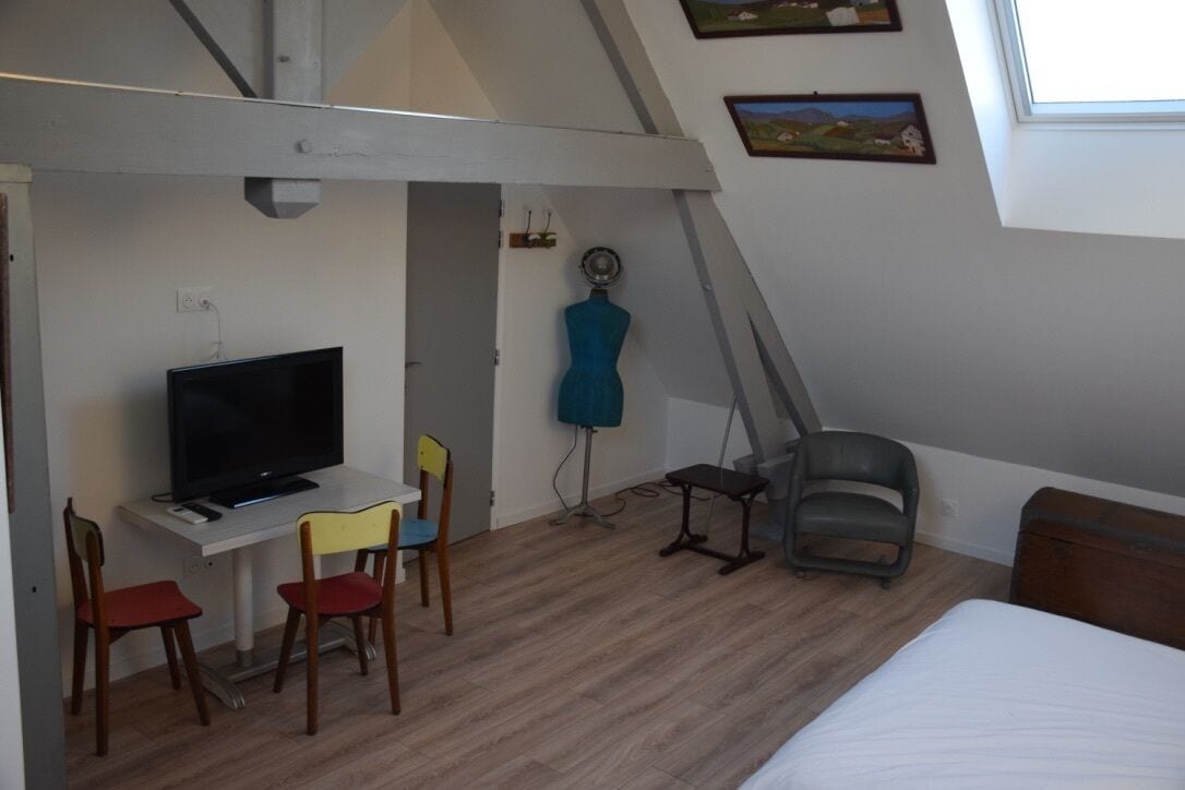 Una habitación pequeña y funcional con cama, escritorio con televisor y una silla.