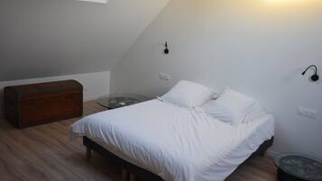 Un dormitorio con una cama, un baúl de madera, una mesa de vidrio y una lámpara de pared.
