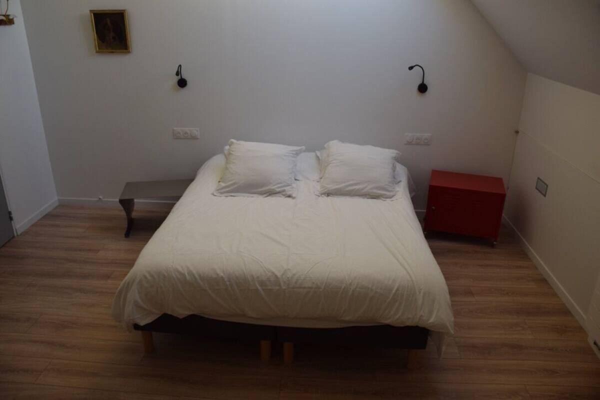 A bedroom with a bed, a bench, a red cabinet, and a wall-mounted light fixture.