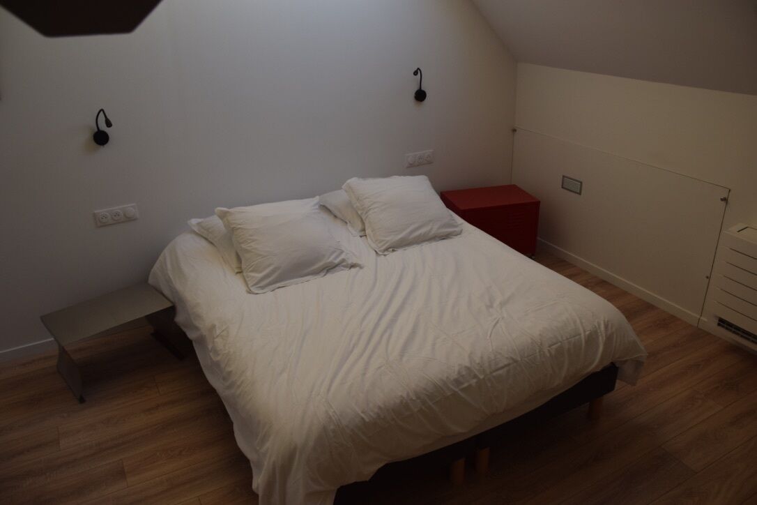 A bedroom with a bed, bedside tables, and a red nightstand.