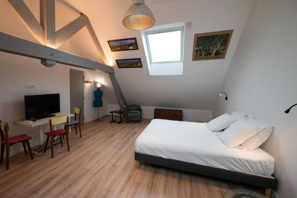 A bedroom with a bed, a desk with a TV, a chair, and a window.