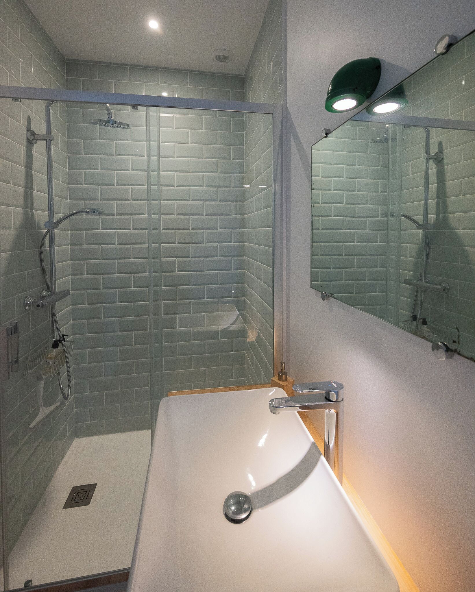Un baño con cabina de ducha de vidrio, un lavabo blanco y un espejo con luz verde.