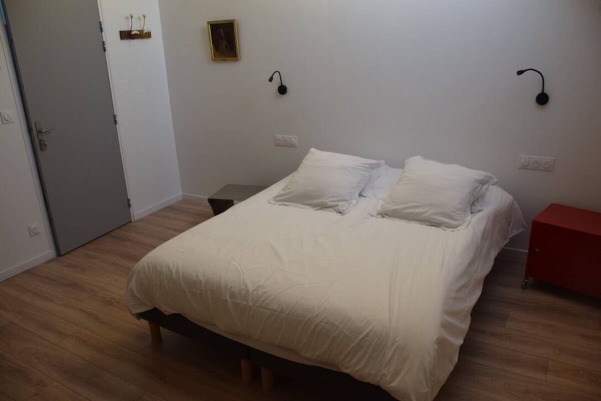 A bedroom with a bed, wooden flooring, a door, and a red cabinet.