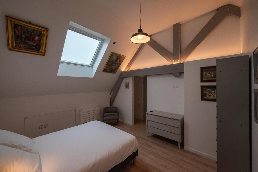 A bedroom with a sloped ceiling, a skylight, a bed, a dresser, and a chair.