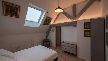 A bedroom with a sloped ceiling, a skylight, a bed, a dresser, and a chair.