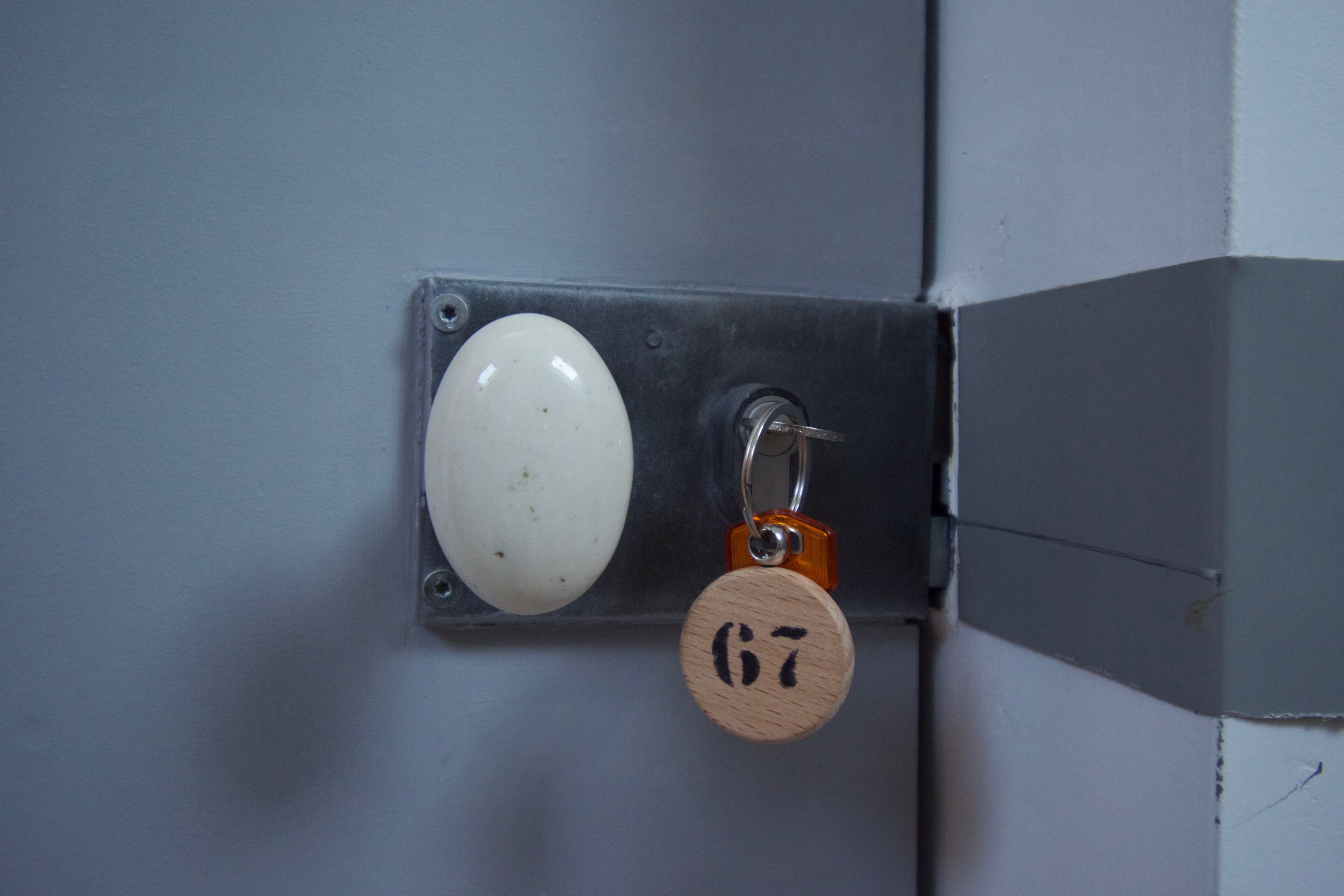 Una puerta con picaporte blanco y cerradura, protegida por una placa metálica y una etiqueta de madera con un llavero.