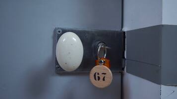 A door with a white handle and a keyhole, secured by a metal plate and a wooden key tag.