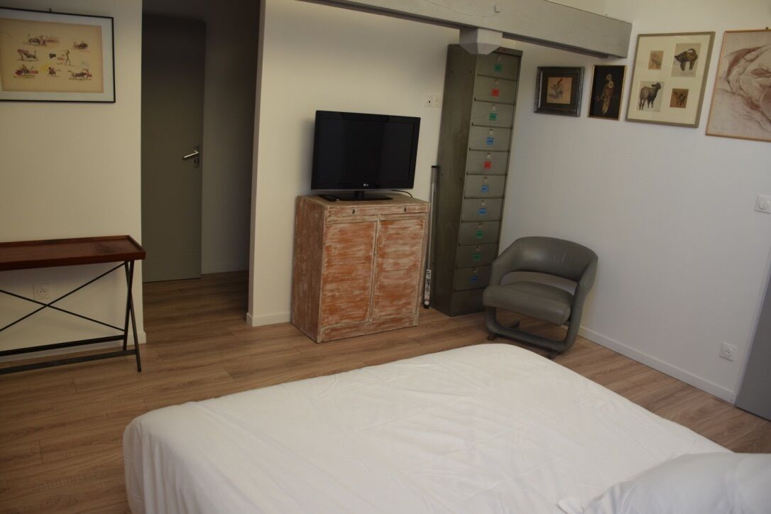 Une chambre à coucher avec un lit, un téléviseur posé sur un meuble en bois, une chaise et une armoire avec un miroir.