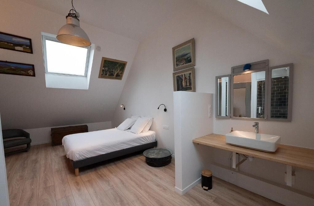 Un dormitorio con cama, mesita de noche, ventana, espejo y una pequeña mesa redonda.
