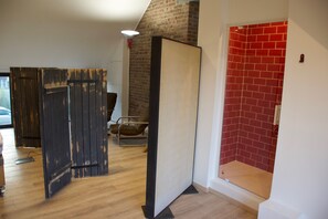 A room with a wooden floor, a brick wall, and a red door.