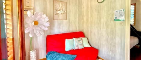 Una habitación acogedora con un sofá rojo, una gran decoración floral blanca, un reloj en la pared y un letrero que dice 'BIENVENUE'.