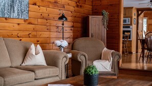 A cozy living room with a wooden wall, a sofa, a chair, a small table with a plant, and a lamp. - 4BR Waterfront Escape w/Woodstoves & Large Dock (Algonquin Highlands)