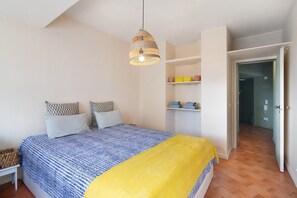 A bedroom with a bed, a hanging light fixture, a shelf with items, and a door leading to another room. - Apartamento Davasa – Close to the Beach (Armação de Pêra)