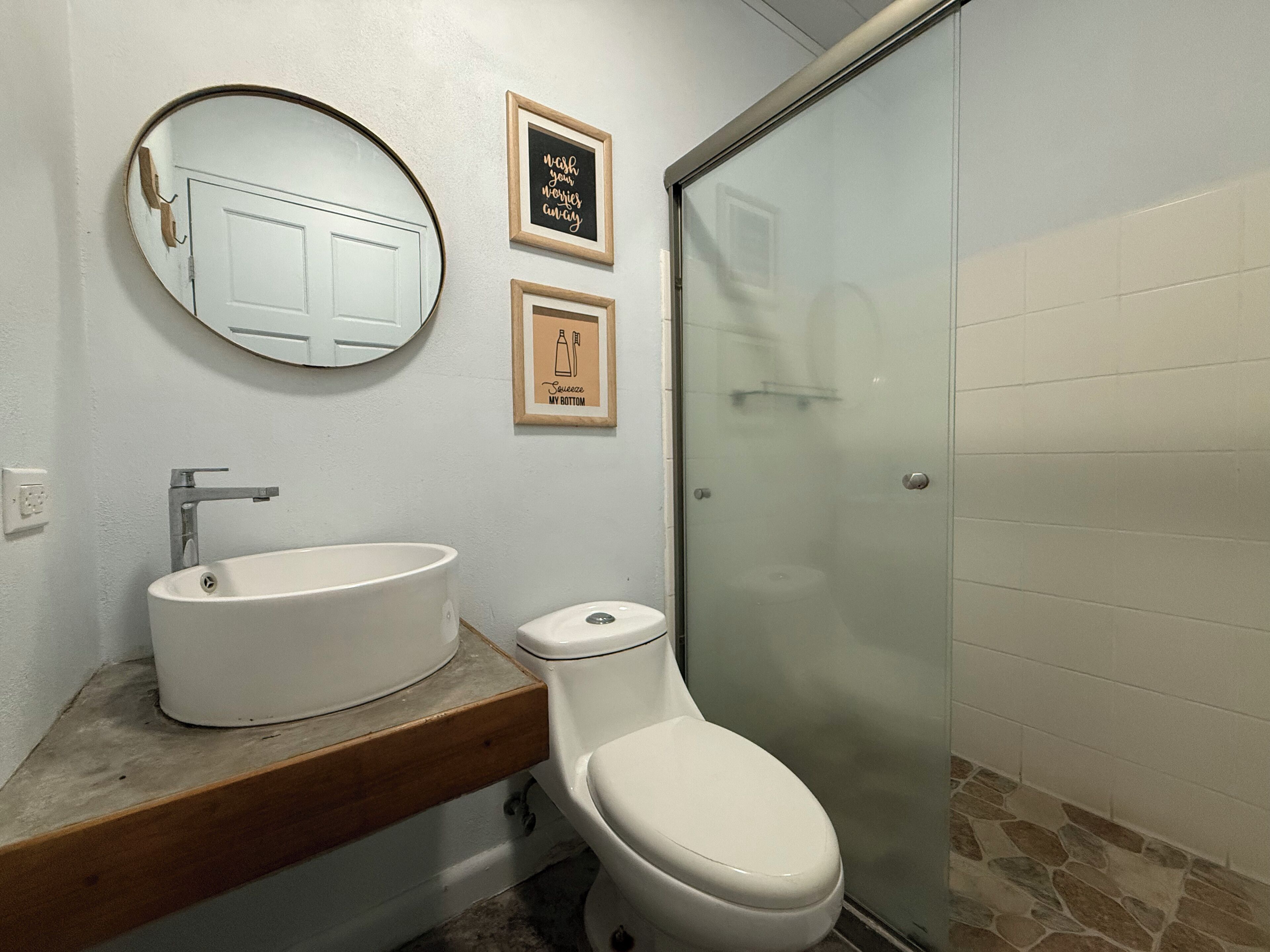 A bathroom with a white sink, toilet, and a glass shower enclosure. There are two framed signs on the wall.
