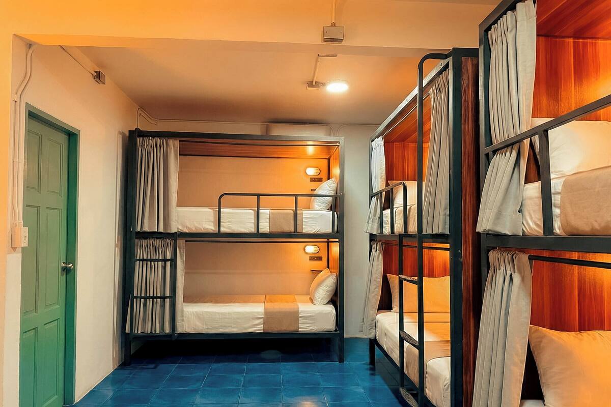 Une chambre de dortoir avec des lits superposés, une porte verte et un sol carrelé de carreaux bleus.