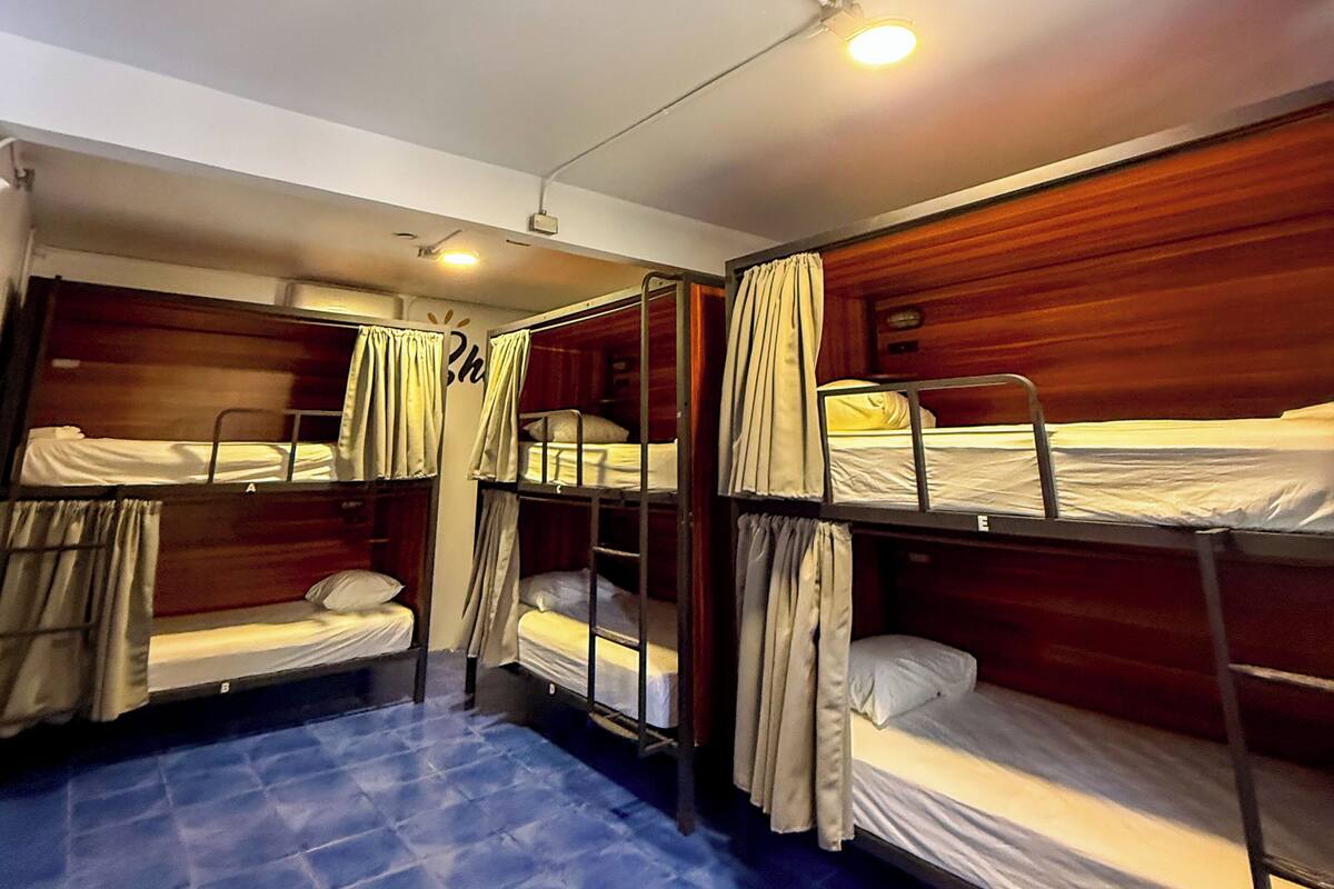 Une chambre avec des lits superposés, des murs en bois, des rideaux et un sol carrelé de carreaux bleus.