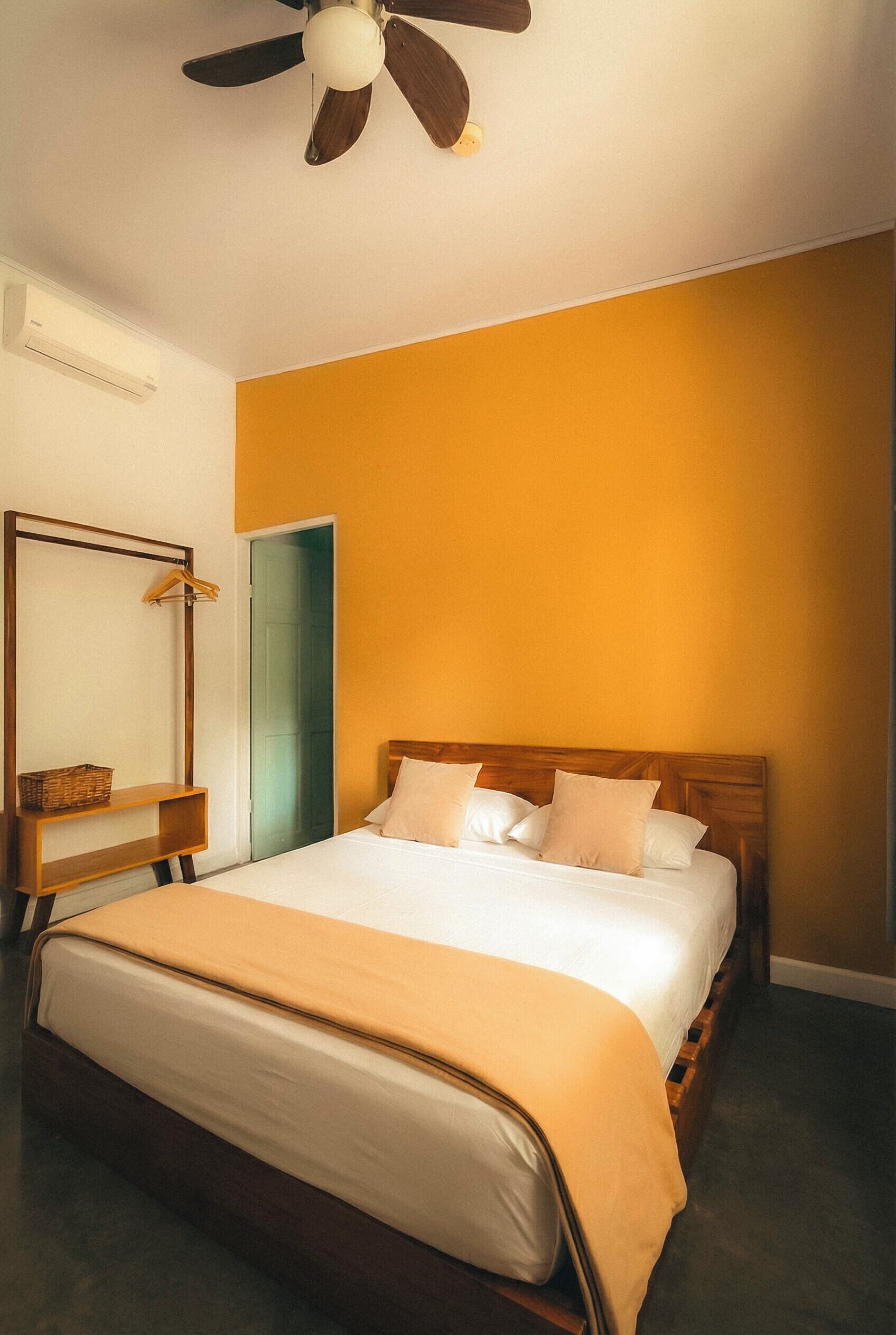 A bedroom with a bed, a wooden headboard, a ceiling fan, a mirror, and a wardrobe.