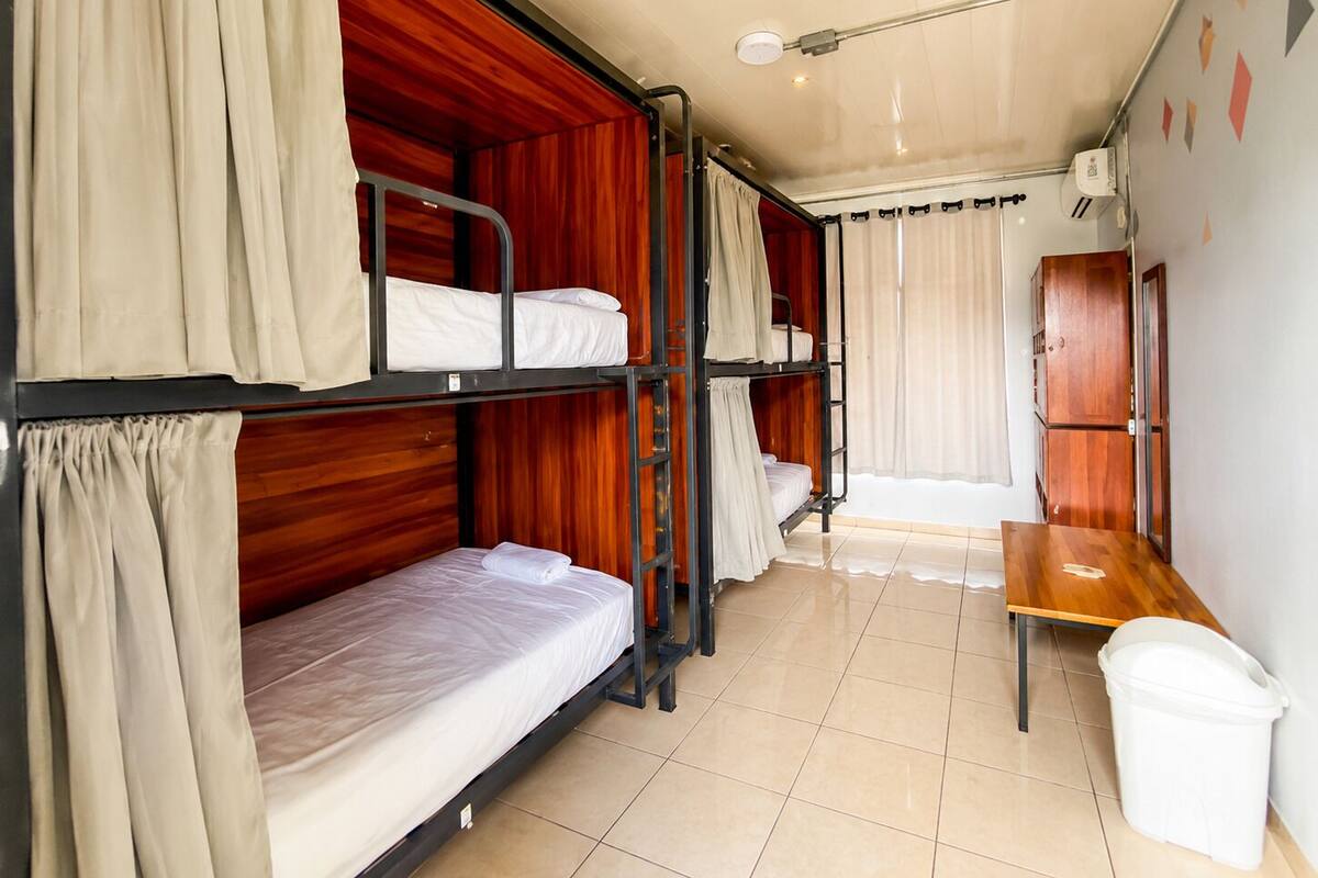 Une chambre avec un lit superposé, un bureau en bois et une poubelle.