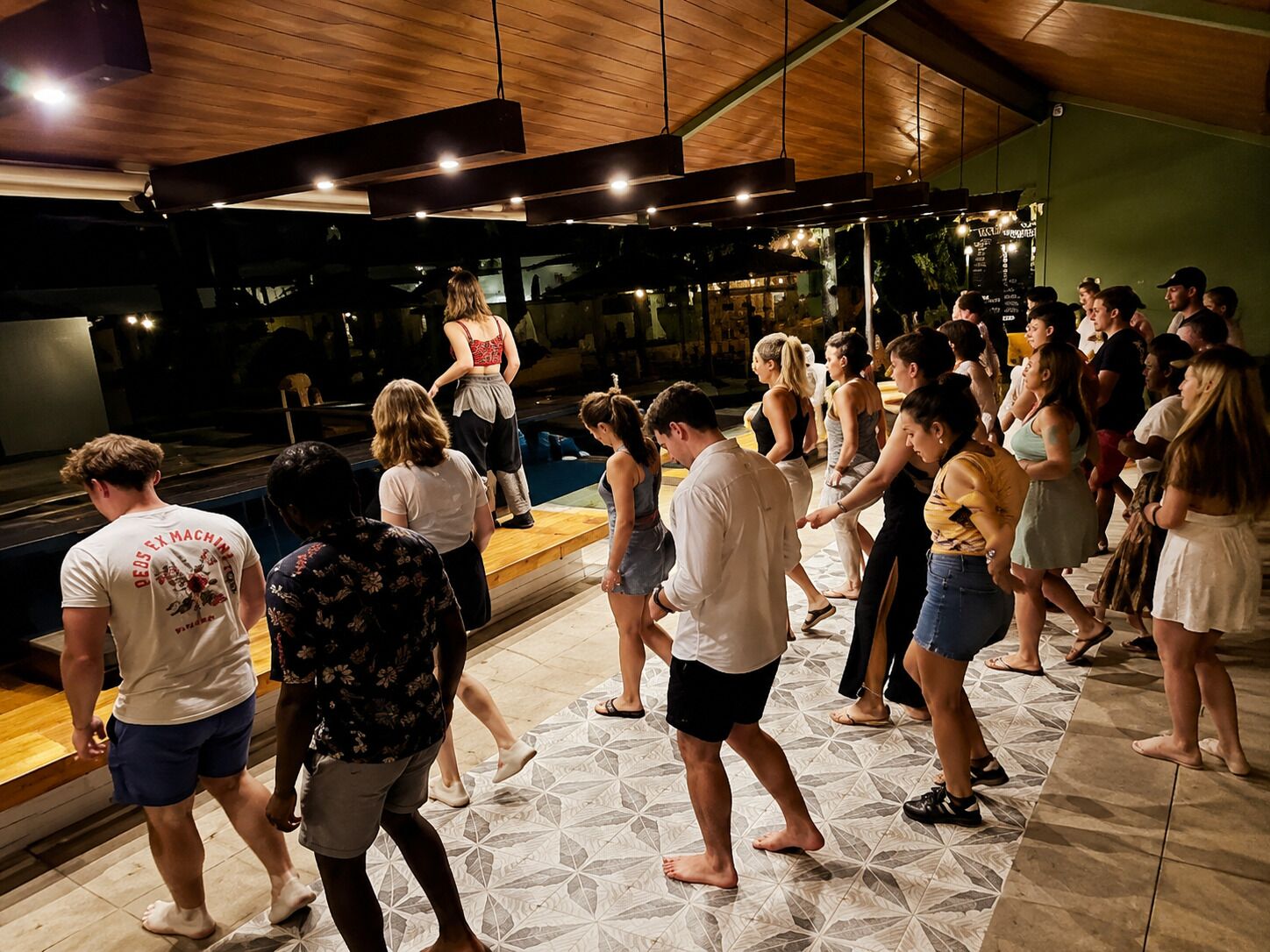 A group of people dancing in a room with a wooden ceiling and tiled floor.