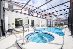 Ein Schwimmbad mit Glasüberdachung, eine überdachte Terrasse und ein weißes Gebäude mit einem Kachelhausdach.
