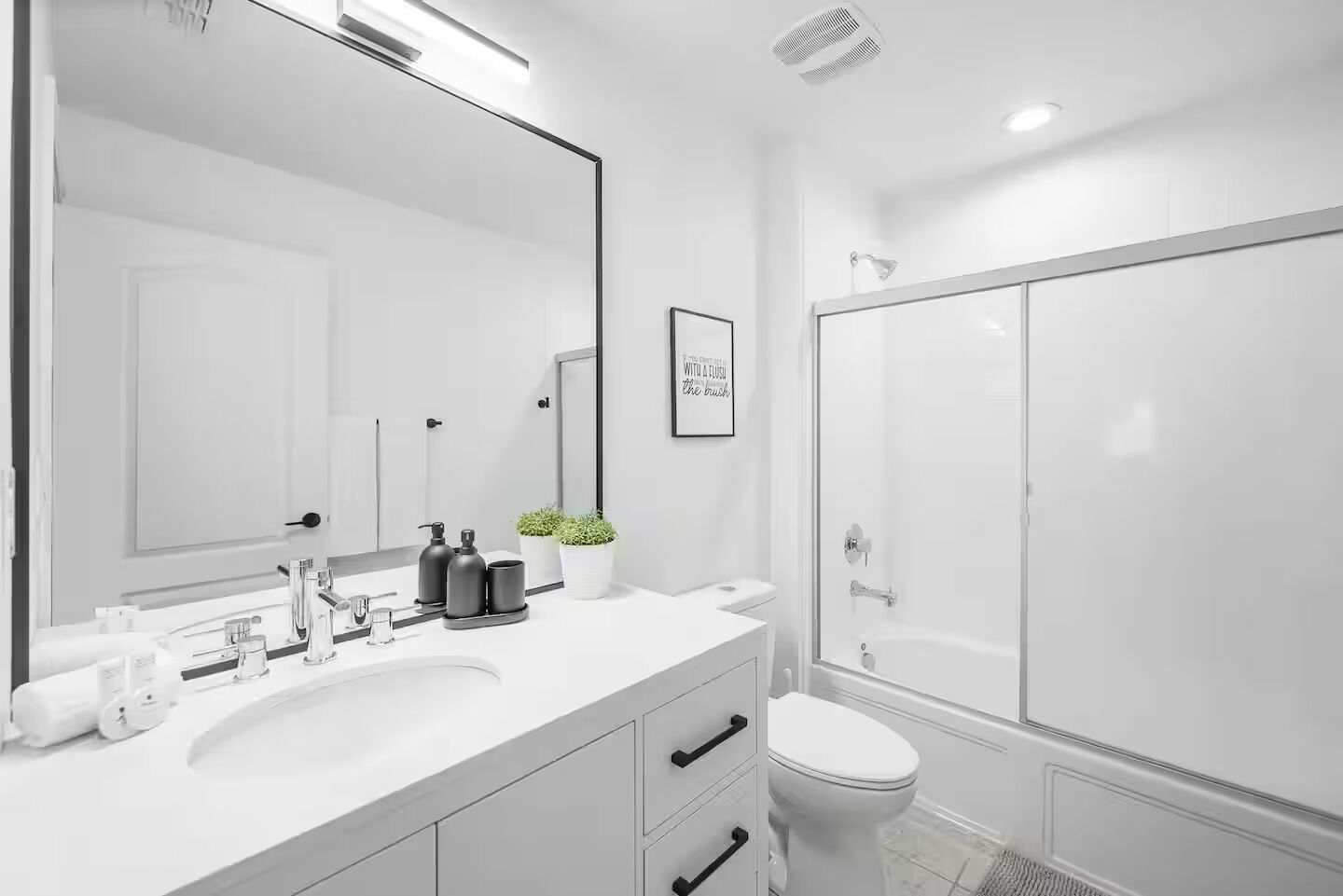 A modern bathroom with a large mirror, white sink, and a glass-enclosed shower.