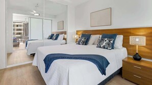 A modern hotel room with a large bed, a wooden nightstand, a ceiling fan, and a large mirror. - Marina Vista—Waterfront Stay near Dining & Markets (Cairns)