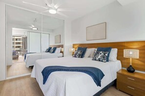 Ein modernes Hotelzimmer mit einem großen Bett, einem Nachttisch aus Holz, einem Deckenventilator und einem großen Spiegel.