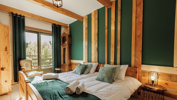 A wooden-framed bedroom with a large bed, two pillows, a nightstand, and a window with curtains. - Jesteśmy Na Ty Apartamenty Lewin Kłodzki (gmina Lewin Kłodzki)