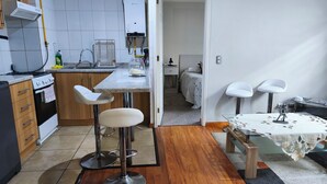 Une cuisine moderne équipée d’une cuisinière à gaz, d’un four encastré et d’un chauffe-eau. On y trouve également un coin repas avec une table et deux tabourets de bar.