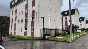 Un immeuble résidentiel à plusieurs étages, doté d’une façade rouge et blanche, d’une entrée sécurisée et d’un espace verdoyant délimité par une clôture blanche.