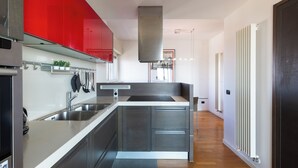 A modern kitchen with stainless steel appliances, a red accent wall, and a built-in island. - notaMI - Settimo Cielo - San Cristoforo (Milan)