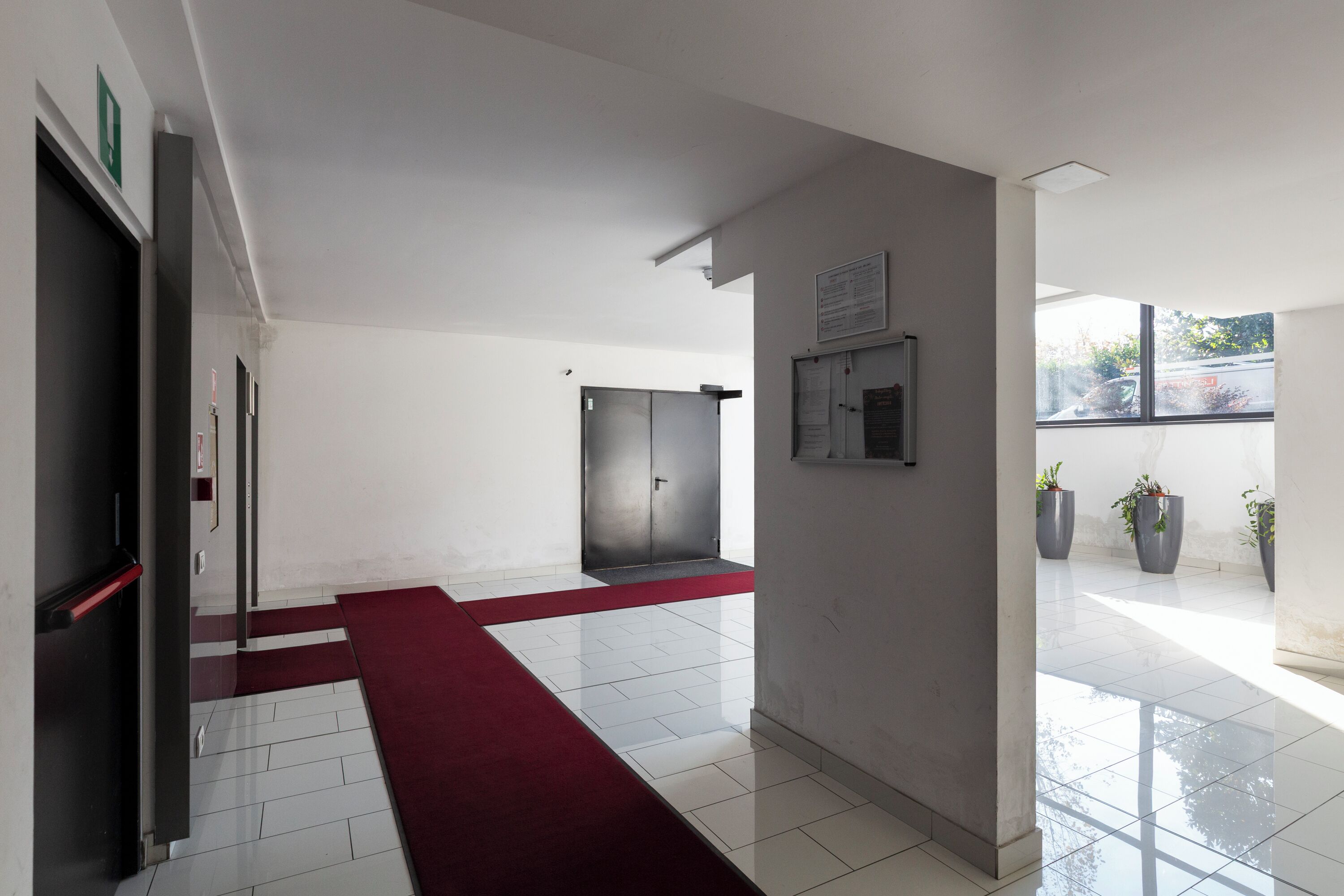 A modern hotel lobby with a red carpet, a reception desk, and a large window offering a view of the parking area.