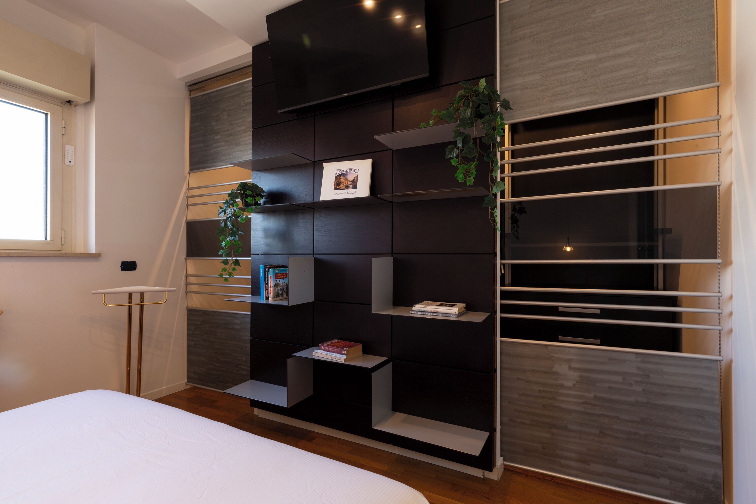 A modern bedroom with a bed, built-in shelving, and a TV.