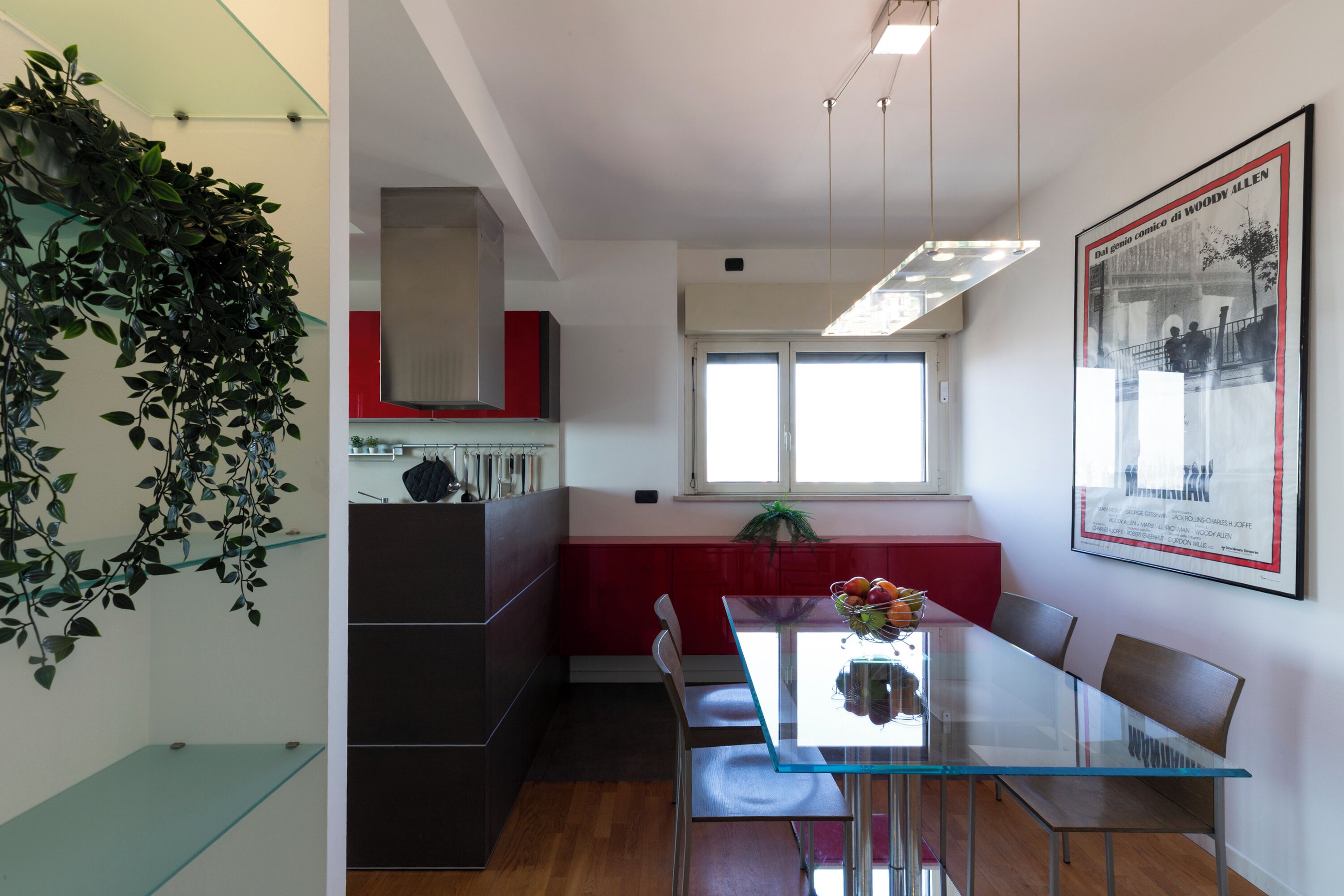 Una cocina moderna con una mesa de comedor de vidrio, armarios rojos y una planta colgante.