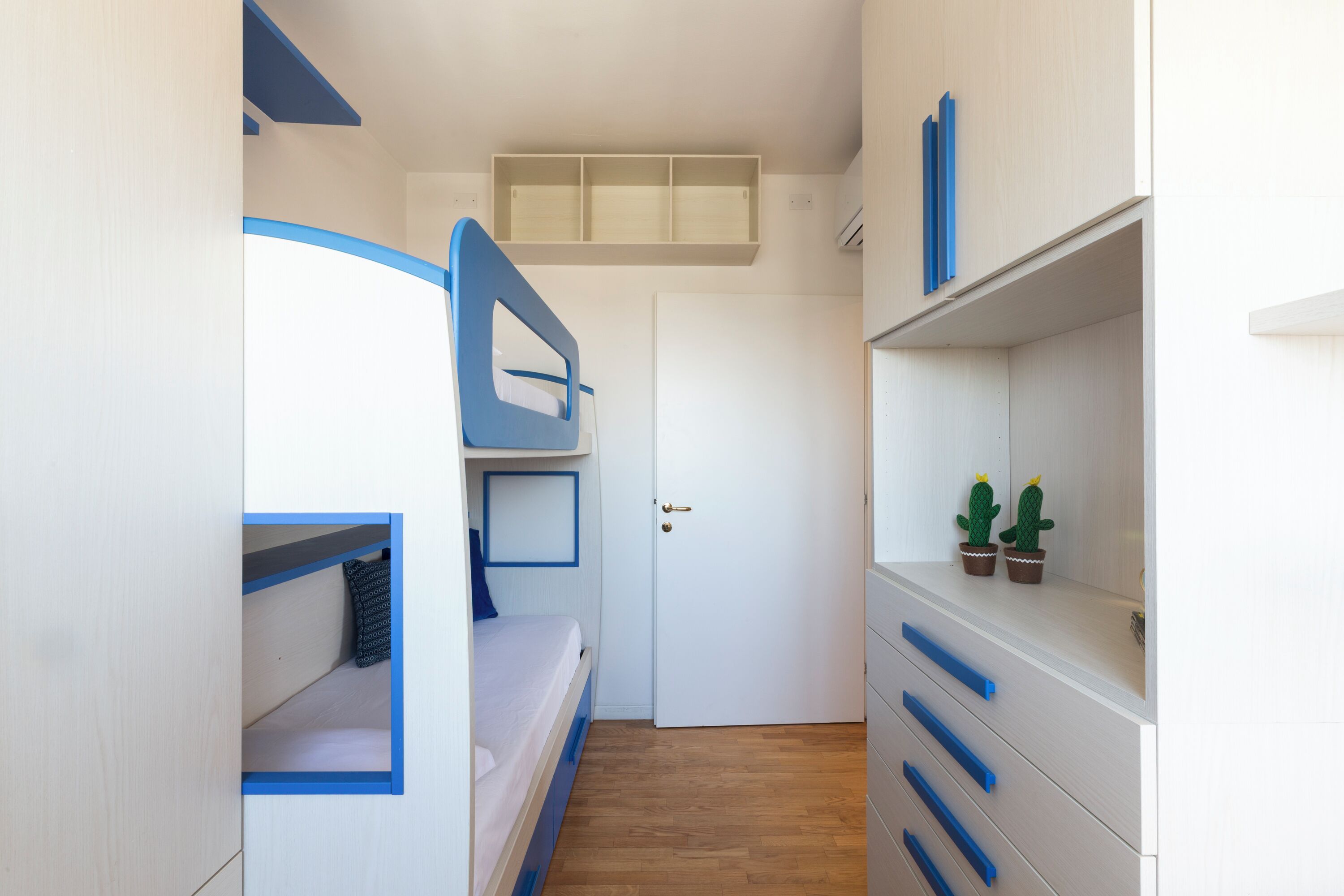 Een kamer met stapelbedden, een witte deur en een plank met potplanten.