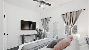 Een moderne slaapkamer met een bed, een televisie, een plant en een plafondventilator.
