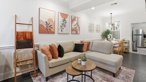 Een moderne woonkamer met een beige hoekbank, een houten ladder en een ronde salontafel met een plant.
