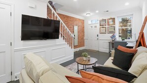 Een woonkamer met een televisie, een trap, een eethoek en een raam met schaakpatroon decoraties.