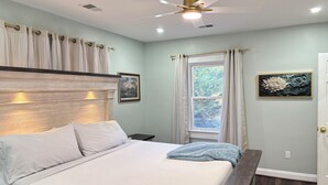 Una camera da letto con un letto, una ventola a soffitto, una finestra con tende e opere d'arte alle pareti.