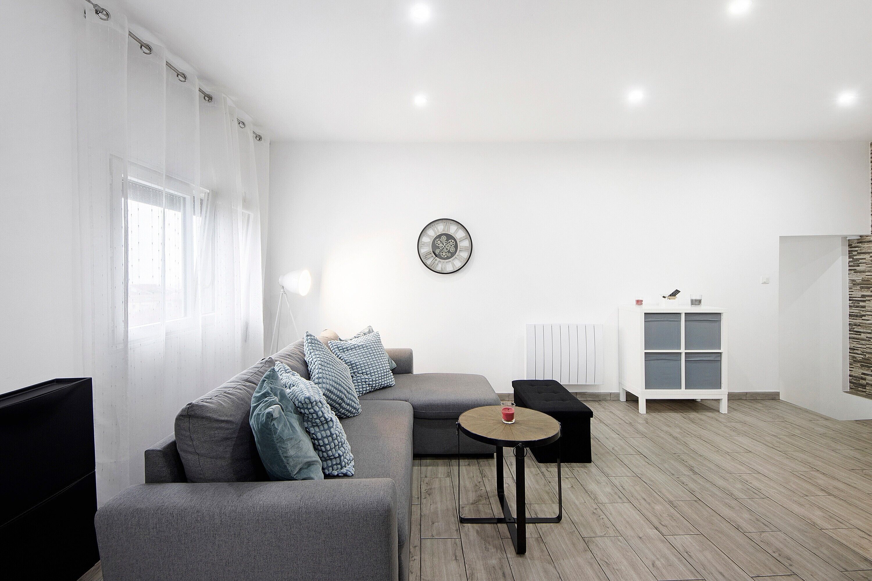 Een moderne woonkamer met een grijze bank, een ronde salontafel en een witte kast.