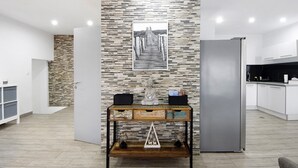 Eine moderne Küche mit Kühlschrank, einem Holztischchen mit Dekoration und einer Wand mit Steinmuster.