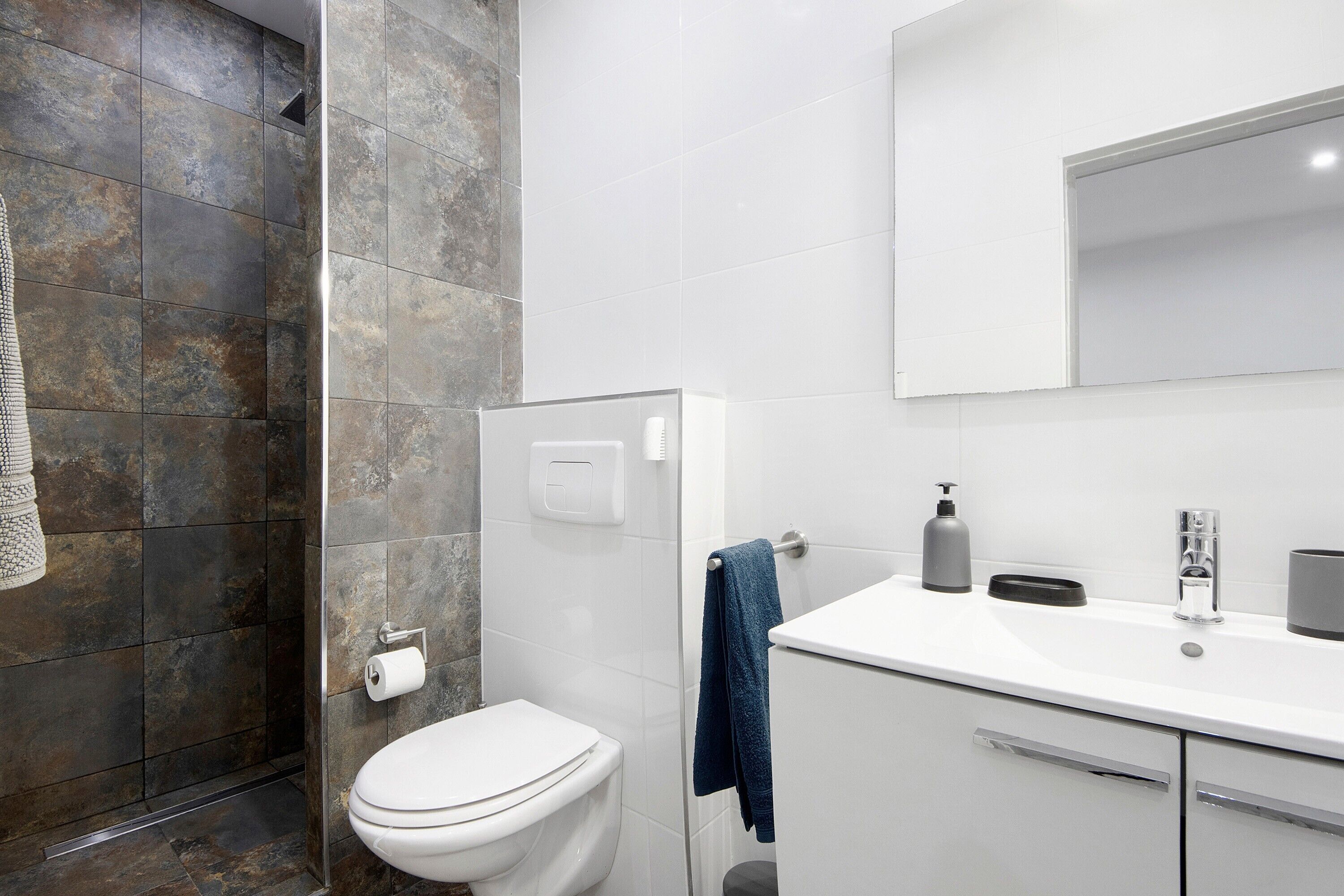 A bathroom with a toilet, a towel rack, a sink with a mirror, and a shower area.