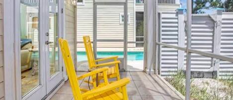 A covered patio with yellow chairs and a view of a house and swimming pool.